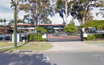Corinda State High School entrance with gated access, featuring surrounding greenery and outdoor sports facilities,