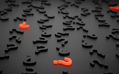 Question marks scattered on a dark surface, with a prominent orange question mark, symbolizing inquiries