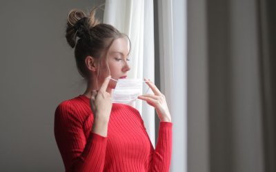 Woman in red sweater adjusting a face mask near a window, emphasizing indoor air quality