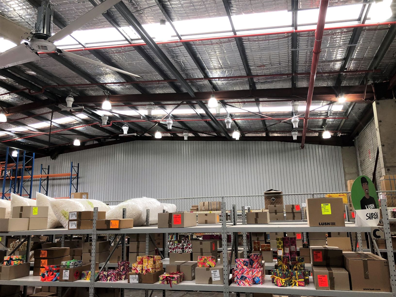 Warehouse ceiling with Airius destratification fans and shelving with stored goods.